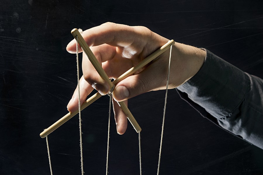 A close-up shot of a hand holding the strings of a marionette.